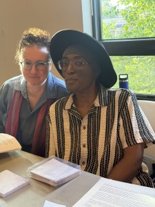 Stuff Studio, a Black human in a wide hat, and Rachel Gold, a white human with curly hair, smiling